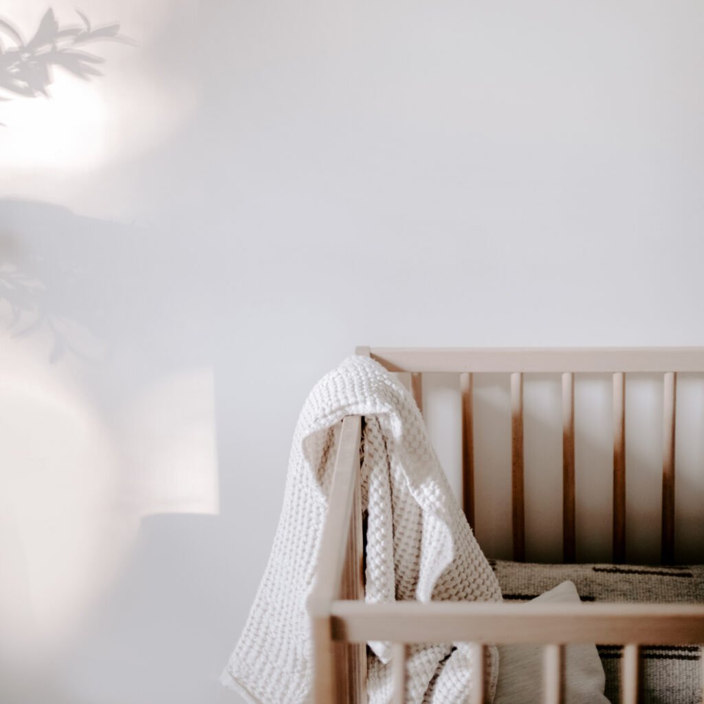 Minimalist wooden crib with a soft knit blanket draped over the edge, bathed in natural morning light — calm, cozy, and serene nursery scene.